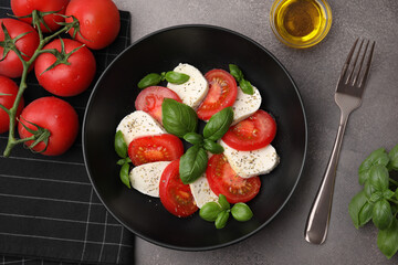 Delicious salad Caprese with tomatoes, mozzarella, basil and spices served on brown table, flat lay