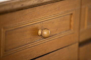 Close up of a wooden chest of drawers with a brass handle
