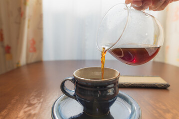 陶器のコーヒーカップにドリップしたコーヒーを注ぐ様子