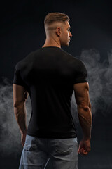 Athletic sexy man in black t-shirt and jeans posing in studio back view - obrazy, fototapety, plakaty