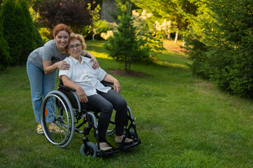 Fototapeta na wymiar Caucasian woman hugging an elderly mother sitting in a wheelchair. Walk outdoors. 