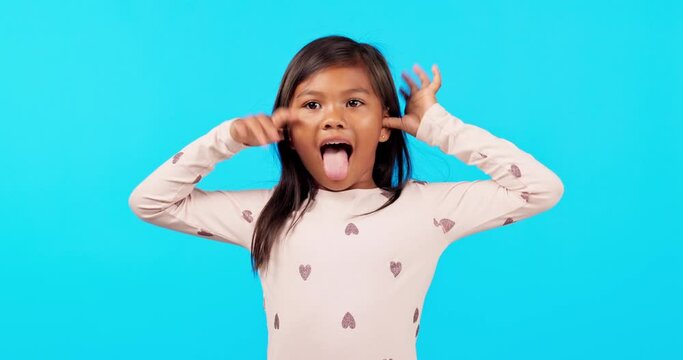 Funny face, tongue out and girl child in studio with crazy, comic and expression on blue background. Silly, portrait and kid person with emoji, personality or fool gesture, playing and goofy fun