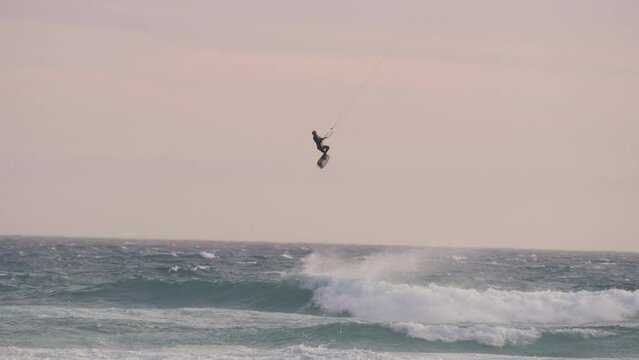 Kite surfing jumping high over a wave in the ocean