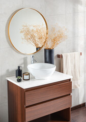 a modern white wash basin situated beneath a round mirror and a wooden cabinet into a bathroom
