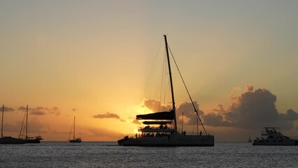 Party boat cruising at sunset, in Saint Lucia, Caribbean. Slow motion of catamaran passing by on a calm evening. Yacht in golden hour with beautiful sun rays, captured in 4K, 60fps slowed to 30fps. - Powered by Adobe
