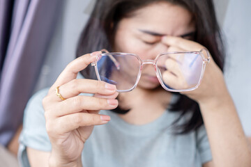 Asian Woman suffering Tired Eyes, Blurred Vision, Double Vision, and Headache, Holding Eyeglasses