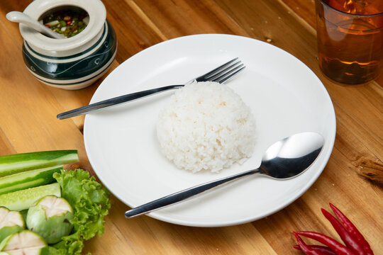 set of white ceramic plate with rice spicy saurce fork and spoon on wood table with copy space