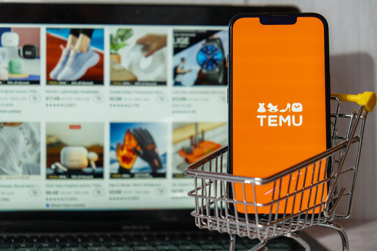Gdansk, Poland - March 2023 Temu app icon in screen of MacBook Apple computer laptop and mobile Iphone with shopping cart. Temu subsidiary of China based e-commerce platform Pinduoduo. Online shopping
