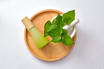 Top view of green bottle with fish mint leaves, mortar and pestle placed on wooden tray on white background. By calming cytokines, fish mint can strengthen immune systems, support allergy therapies.