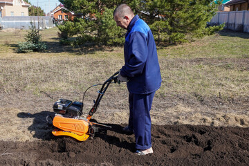 A man works in a vegetable garden in early spring. Digs the ground.  Works as a cultivator, walk-behind tractor.