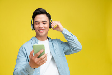  Portrait of overjoyed asian guy singing song and using smart phone as microphone, wearing wireless headset
