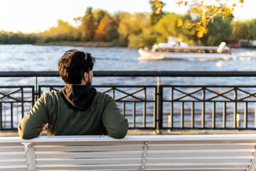 Fototapeta premium Back view of a man sitting on a bench at sunset contemplating the river