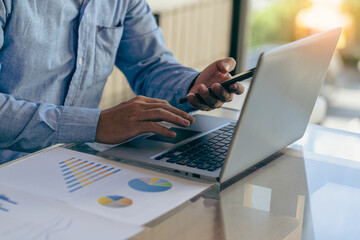 Businessman holding pen pointing to market graph and working on laptop computer working using calculator for mathematics on wooden table at office finance concept close up pictures