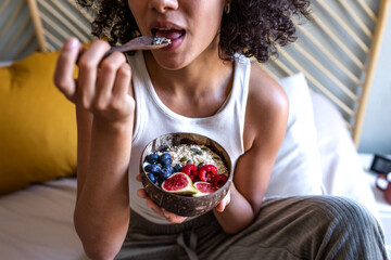 Unrecognizable young multiracial woman eating healthy breakfast bowl of oats and fruit. Breakfast...