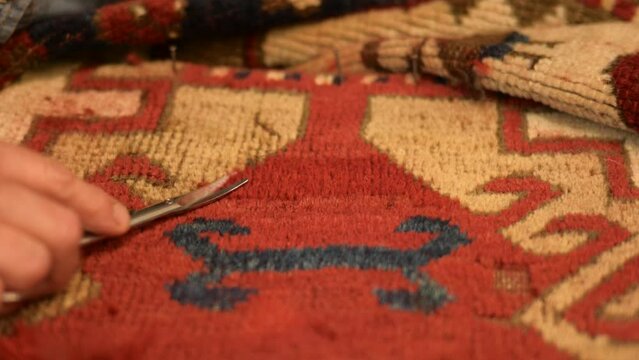Woman restoring an Antique Oriental Rug. Detailing the new knots with a scissor.