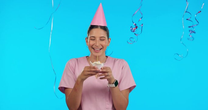 Birthday, party and balloons with a nurse woman in studio isolated on a blue background for celebration. Smile, healthcare and a happy female medicine professional blowing out a candle on a cupcake