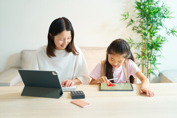 Obraz premium タブレットPCを使って仕事をする女性と遊ぶ女の子