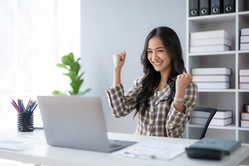 Happy asian businesswoman raising hands with victory smiling happily with laptop computer. The...