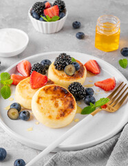 Cottage cheese pancakes, syrniki, ricotta fritters with fresh berries, honey and sour cream on a gray concrete background. Healthy and delicious breakfast. Top view, copy space.