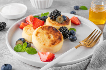Cottage cheese pancakes, syrniki, ricotta fritters with fresh berries, honey and sour cream on a gray concrete background. Healthy and delicious breakfast. Top view, copy space.