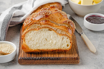 Homemade challah bread with sesame seeds, butter and jam on a grey concrete background. Sweet bread. Selective focus.