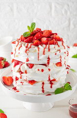 Pavlova layered cake with fresh strawberries, sauce and whipped cream on a white wooden background. Summer beautiful cake. Selective focus.
