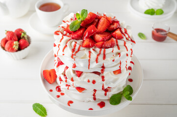 Pavlova layered cake with fresh strawberries, sauce and whipped cream on a white wooden background. Summer beautiful cake. Selective focus.