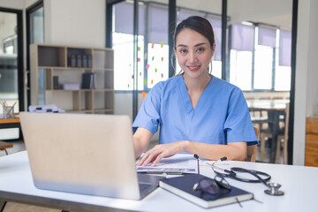 Happy doctor Portrait of young asian woman nurse or doctor smiling using a laptop writing content at consultation	