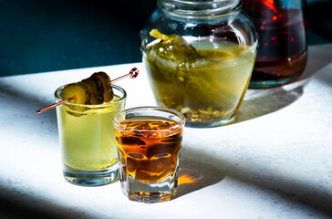 Pickleback, alcoholic cocktail drink from cucumber pickle and whiskey in small shot glasses. Hard light and shadow pattern, green background