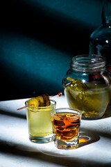 Pickleback, alcoholic cocktail drink from cucumber pickle and whiskey in small shot glasses. Hard light and shadow pattern, green background