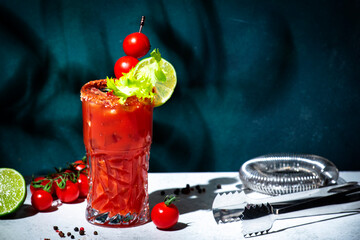 Bloody Mary cocktail drink with tomato juice, vodka, lemon, celery, hot sauce and ice in glass garnished with salt and ground chili pepper. Dark green background, hard light and shadow pattern