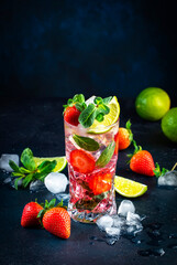 Summer strawberry mojito cocktail with lime, white rum, soda, cane sugar, mint, and ice in glass on deep blue background. Cold refreshing beverage