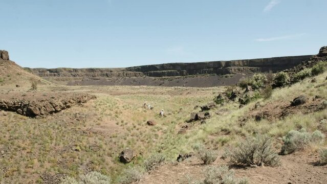 Hikers enjoy dry grass basin below Dry Falls in Washington Scablands