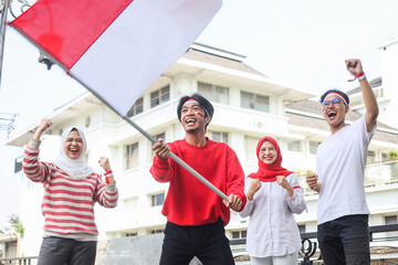 Excited young man waving the flag while the others raising arm on Indonesian independence day...