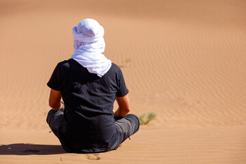 Caucasian man with white turban sitting and looking at the desert