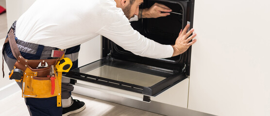 Professional serviceman repairing modern oven in kitchen