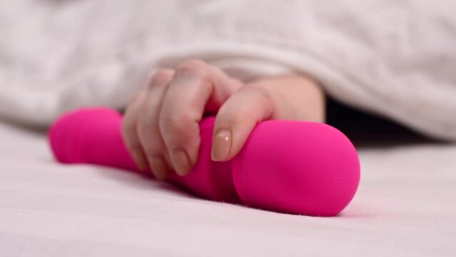 Woman taking pink vibrator lying under white blanket. 