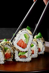 One Philadelphia roll in sesame with salmon grasped from plate by chopsticks