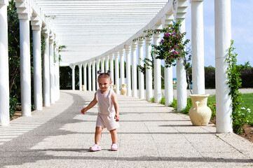 A little girl runs along the alley with white columns in summer. Concept of a happy childhood, parenthood, and happy family. Concept of tourism and recreation