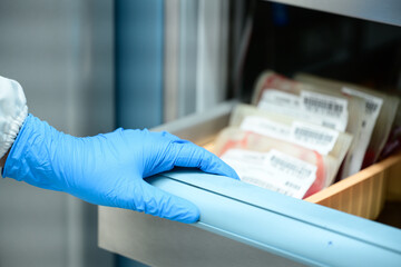 Close up scientist hand holding red blood bag in storage refrigerator at blood bank unit...