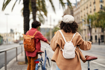 Rear view of two travelers pushing their bikes on the city street in Spain.