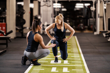 Female coach is helping a sportswoman with lunges exercises in a gym.