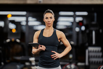 Portrait of a serious female trainer holding tablet and looking at the camera.