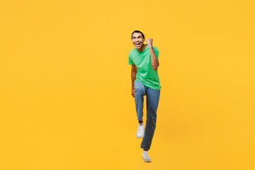Fototapeta na wymiar Full body young man of African American ethnicity he wears casual clothes green t-shirt hat doing winner gesture celebrate clenching fists say yes isolated on plain yellow background studio portrait.