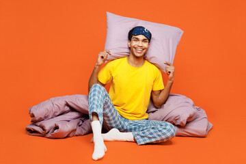 Full body smiling happy fun young man wear pyjamas jam sleep eye mask sit with pillow duvet blanket...