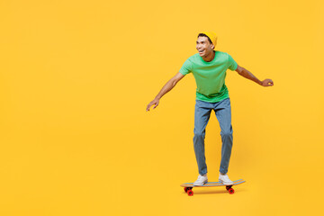 Fototapeta na wymiar Full body side view smiling young man of African American ethnicity he wears casual clothes green t-shirt hat rising skateboard isolated on plain yellow background studio portrait. Lifestyle concept.