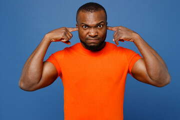 Young sad man of African American ethnicity wear orange t-shirt cover ears with hands fingers do not want to listen scream isolated on plain dark royal navy blue background studio Lifestyle concept