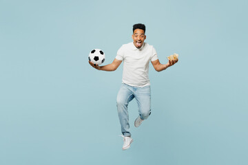 Fototapeta na wymiar Full body excited young man fan wear t-shirt cheer up support football sport team hold in hand chips in bowl soccer ball jump high watch tv live stream isolated on plain pastel blue color background.