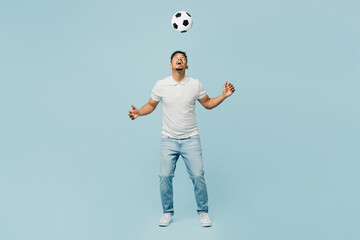 Full body cheerful happy active young man fan wearing t-shirt cheer up support football sport team hit soccer ball on head watch tv live stream isolated on plain pastel light blue color background.