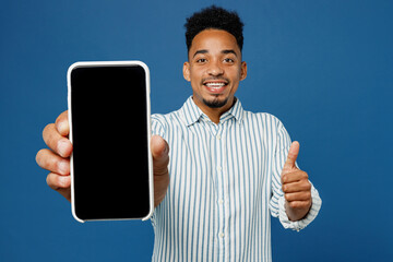 Young man of African American ethnicity wear casual clothes shirt hold in hand use mobile cell phone with blank screen workspace area show thumb up isolated on plain dark royal navy blue background.